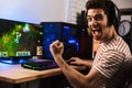 Portrait of ecstatic gamer guy in headphones screaming and rejoicing, while playing video games on computer