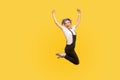 Portrait of ecstatic lively energetic hipster girl jumping in air celebrating victory. yellow background, studio shot