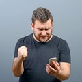 Portrait of ecstatic man holding cell phone and celebrating with closed fist against gray background