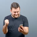 Portrait of ecstatic man holding cell phone and celebrating with closed fist against gray background Royalty Free Stock Photo