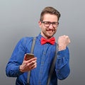 Portrait of ecstatic man holding cell phone and celebrating with closed fist against gray background Royalty Free Stock Photo