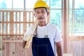 Portrait of elderly Asian carpenter with mustache wearing antiknock helmet and cloth gloves, holding wooden plank, senior Royalty Free Stock Photo