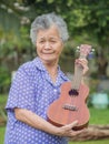 Portrait of an elderly Asian woman holding a ukulele, smiling and looking at the camera while in a garden. Royalty Free Stock Photo