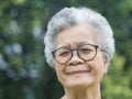 Portrait of an elderly Asian woman with short gray hair, wearing glasses, smiling and looking at the camera while standing in a Royalty Free Stock Photo