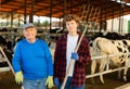 Portrait of an elderly dairy farm owner and his young assistant grandson against the background of cows in stall