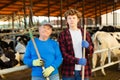 Portrait of an elderly dairy farm owner and his young assistant grandson against the background of cows in stall