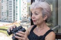 Portrait of an elderly, fastidious woman of 60-65 years with binoculars against the backdrop of the urban landscape.Concept: spyin Royalty Free Stock Photo