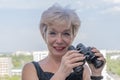 Portrait of an elderly, fastidious woman of 60-65 years with binoculars against the backdrop of the urban landscape.Concept: spyin Royalty Free Stock Photo