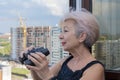 Portrait of an elderly, fastidious woman of 60-65 years with binoculars against the backdrop of the urban landscape.Concept: spyin Royalty Free Stock Photo