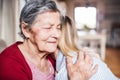 An elderly grandmother with an adult granddaughter at home, hugging.