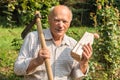 Portrait of elderly man with ax on his shoulder and a half of wood in his hand in the garden