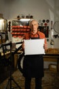 Portrait of elderly man with empty blank mock-up poster. Male mechanic in garage interior or workshop. Bike service Royalty Free Stock Photo