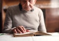 Portrait of elderly man sitting at the table indoors at home, resting and reading bible. Royalty Free Stock Photo