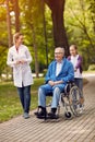 portrait of elderly man on wheelchair with nurse and granddaughter outdoor. Royalty Free Stock Photo