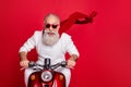 Portrait of elderly modern person in eyewear eyeglasses driving his bike wearing white sweater isolated over red