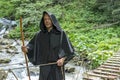 Portrait of an elderly monk 45-50 years old with a beard in a black cassock with a staff walking on a suspended wooden bridge over