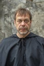 Portrait of an elderly monk 45-50 years old with a beard in a black robe on the background of a textured wall, looking directly in Royalty Free Stock Photo