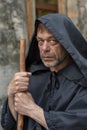 Portrait of an elderly monk 45-50 years old with a beard in a black robe with a staff on the background of a textured wall, lookin