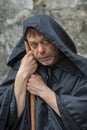 Portrait of an elderly monk 45-50 years old with a beard in a black robe with a staff on the background of a textured wall, lookin Royalty Free Stock Photo