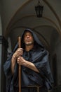 Portrait of an elderly monk 45-50 years old with a beard in a black robe with a staff, standing under the arches of a monastery or Royalty Free Stock Photo