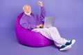 Portrait of elderly retired trendy cheery lucky man pensioner using laptop having fun isolated over bright violet purple