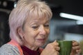 Portrait of an elderly thoughtful stylish woman 60-65 years old with blond hair, in hands holding a tea mug on blurred kitchen bac