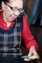 Portrait of an elderly woman with a beautiful wrinkled face in glasses holds pills in her hands to choose medicine. The