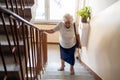 Senior woman climbing staircase with difficulty