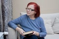 Portrait of elderly woman with closed book in hands, at home, sitting on sofa. Senior woman has finished reading paper book,