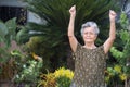 Portrait of an elderly woman exercise while standing in a garden. A beautiful senior woman short with gray hair is happy