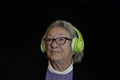 Portrait elderly woman listening music with headphones on black dark background Royalty Free Stock Photo