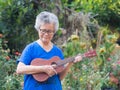 Portrait of elderly woman playing ukulele in her garden. Relaxing by singing and play small guitar happy and enjoy life after Royalty Free Stock Photo