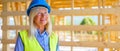 Portrait of elderly woman with protective helmet and yellow vest working at sustainable wooden eco building.