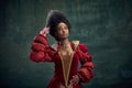 Portrait of elegant african girl, medieval royal person, queen with hair accessories standing against vintage green