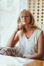 Portrait of elegant attractive blonde Caucasian an aged woman with stylish hair and glasses in white t-shirt sitting at a dining Royalty Free Stock Photo