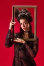 Portrait of elegant, beautiful, young girl with blushing cheeks, posing with picture frame against red background Royalty Free Stock Photo