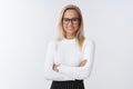 Portrait of elegant blond woman in sweater and glasses standing confident and self-assured over white wall crossed arms Royalty Free Stock Photo