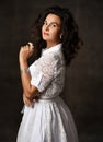 Portrait of elegant brunette woman in white pinup 60th lace dress with short sleeves stands side to looking at camera Royalty Free Stock Photo