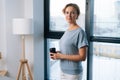 Portrait of elegant business woman holding coffee cup and looking at camera standing on background of large window at Royalty Free Stock Photo