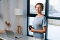 Portrait of elegant business woman holding coffee cup and looking at camera standing on background of large window at Royalty Free Stock Photo