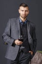 Portrait of elegant confident handsome man in business suit with glass of red wine on gray wall background