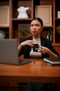 Confident millennial Asian businesswoman holding a cup of coffee, sitting at her office desk Royalty Free Stock Photo
