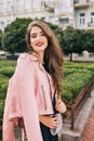 Portrait of elegant girl with long curly hair posing on steer. She wears black dress, pink jacket, clutch bag, red lips Royalty Free Stock Photo