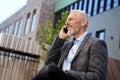 Portrait of elegant mature businessman talking on the phone while taking a break, sitting on the bench outdoors Royalty Free Stock Photo