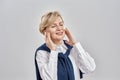 Portrait of elegant middle aged caucasian woman wearing business attire, adjusting her earbuds, smiling with eyes closed Royalty Free Stock Photo