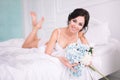 Portrait of elegant woman with curly hair with flowers lies in bed