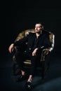 portrait of an elegant young European man in a suit sitting on a chair in a dark interior Royalty Free Stock Photo