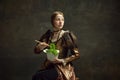 Portrait of elegant young girl, queen in vintage dress eating lettuce with chopstick against dark green background