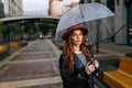 Portrait of elegant young woman in fashion hat standing on beautiful city street with transparent umbrella enjoying Royalty Free Stock Photo