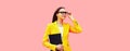 Portrait of elegant young woman with folder looking away wearing eyeglasses, yellow business suit on pink studio background Royalty Free Stock Photo